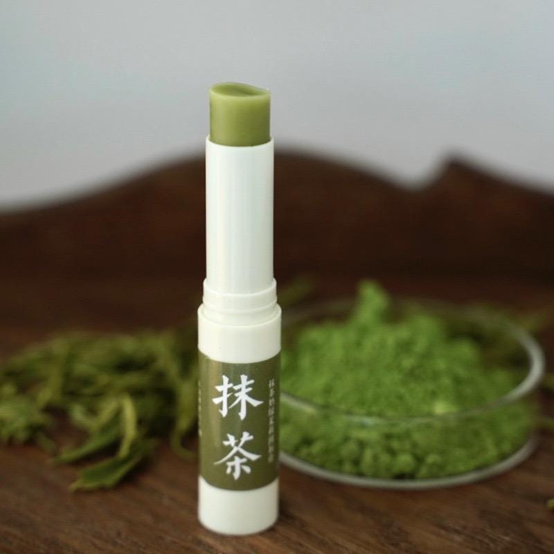 Green lip balm with white cap on a wooden surface with green leaves and powder in the background